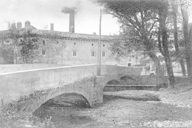 Stadtansicht mit Gebäuden und Bäumen, einem Mast und einer Brücke im Vordergrund, Wasser unten und Rauch, der von der Schornsteinoberseite in den Himmel aufsteigt.