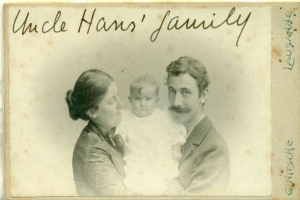 Ein altes Foto eines Mannes im Anzug und Schlips, einer Frau mit einem Baby auf dem Arm und dem Text "Onkel Hans' Familie" oben drauf, alle strahlend.