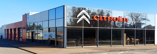 Außenansicht eines Citroën-Händlerbetriebs mit Glaswänden und -türen, einer Straße davor und einem klaren blauen Himmel.