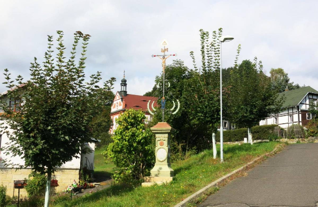 Eine Straße mit einem Kreuz am Straßenrand, umgeben von Gras, Pflanzen, Bäumen, Pfählen, Laternen und Häusern, die zur Kirche des Heiligen Grabes führt.