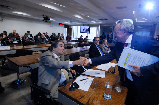 Eine Gruppe von Menschen ist in ein Gespräch vertieft, während andere im Hintergrund sitzen, unter einer Decke mit Beleuchtungskörpern.