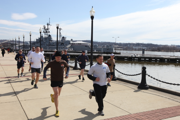 Eine volle Brücke mit laufenden Menschen, Straßenlaternen, Wasser, Bergen und Gebäuden im Hintergrund.