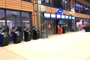 Großer Raum mit mehreren wandmontierten Fernsehern, die ein Sportwetten-System anzeigen, Glasfenster, Deckenbeleuchtung und andere Gegenstände.