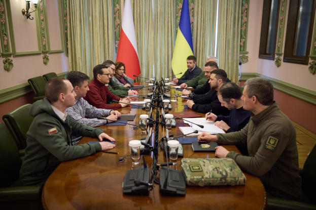 Eine Gruppe von Männern in einer offiziellen Umgebung mit Mikrofonen und Dokumenten an einem Holztisch, die eine Vereinbarung diskutieren, mit Flaggen und Beleuchtung im Hintergrund.