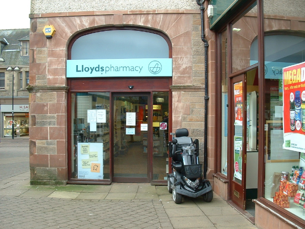 Eine Apotheke mit einem vor dem Gebäude geparkten Auto und einem Gebäude auf der linken Seite.