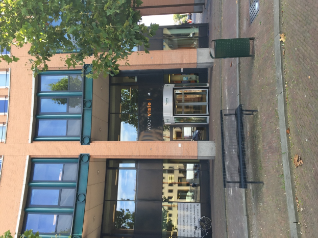 Ein Gebäude mit Mülltonne, Bank, Baum und Fahne davor.