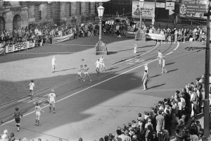 Schwarzes Bild eines auf der Straße gespielten Fußballspiels mit Zuschauern, Laternenpfählen, Gebäuden und Bannern im Hintergrund.