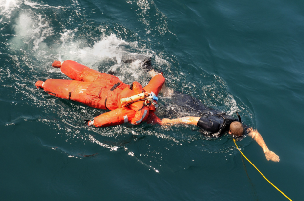 Retter in oranger Lebensweste über einem Gewässer hängend.
