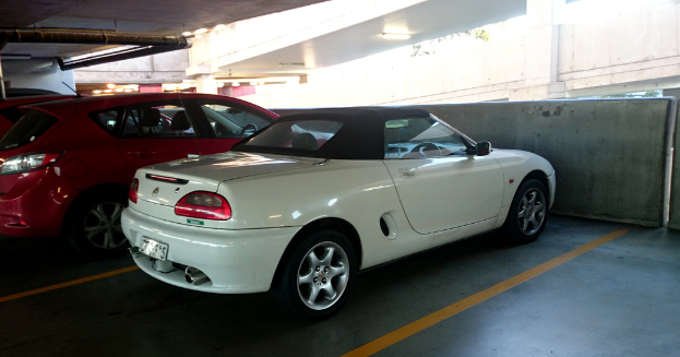 Autos stehen in einem Keller mit einem an das Dach angeschlossenen Rohr und einem weiteren Gebäude auf der rechten Seite.