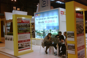 Ein Raum mit Menschen an einem Tisch sitzend, die auf Laptops arbeiten, umgeben von mehreren Flyern mit verschiedenen Anzeigen.