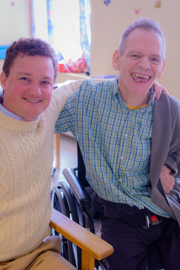 Zwei Männer sitzen auf einem Stuhl und lächeln.