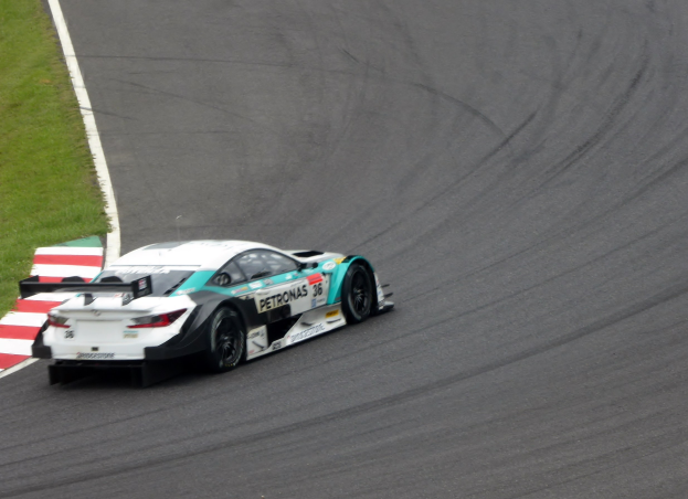 Ein Mercedes-AMG GT3 Rennauto fährt auf einer Rennstrecke mit Text auf der Karosserie und Gras links daneben.