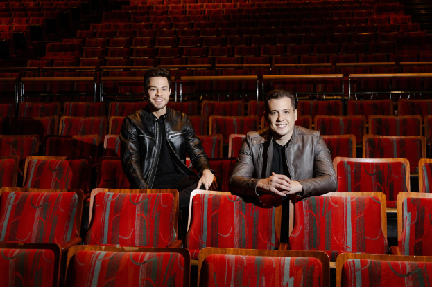 Zwei Männer in schwarzen Jacken, die während einer *Dancing with the Stars*-Vorstellung in roten Auditoriumsitzen lächeln.
