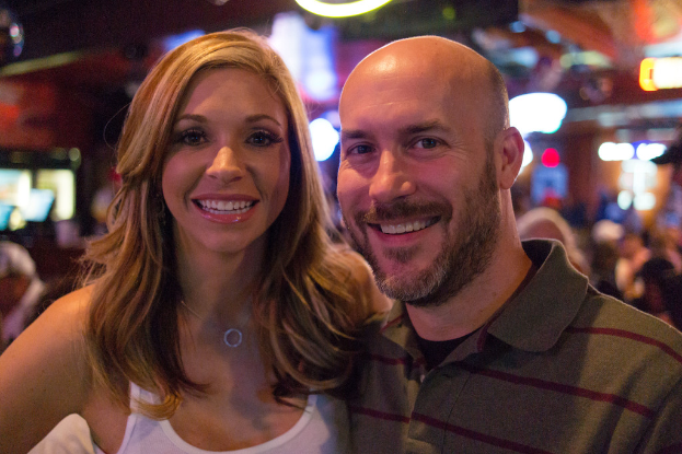 Ein Paar lächelt strahlend in der Vordergrund mit einem unscharfen Hintergrund.