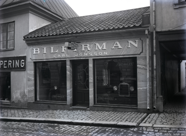 Ein Schwarz-Weiß-Foto eines Gebäudes mit einer "Bilferman"-Aufschrift, Fenstern, einer Tür und Tafeln mit Text sowie einer Straße unten.