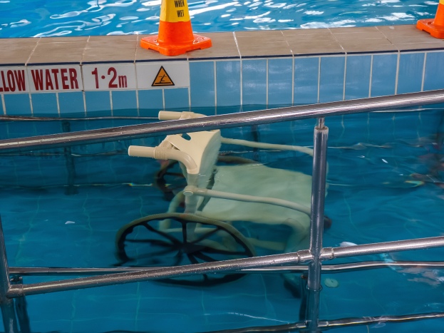 Ein Schwimmbad mit einem Stuhl in der Mitte, umgeben von Sicherheitskegeln und einem Geländer, und ein Schild an der Wand, das auf die Anwesenheit von Schwimmausrüstung hinweist.