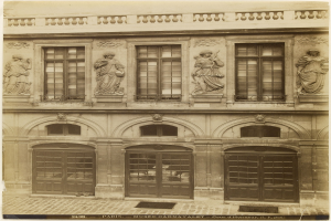 Altes Gebaude mit skulptierter Fassade, Fenstern, Tueren und Text unten.