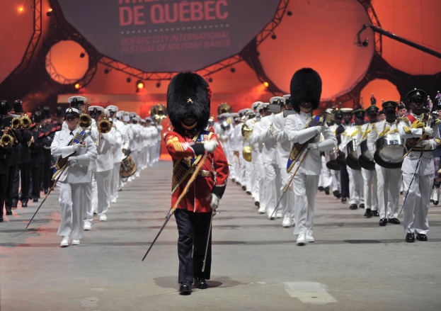 Eine Gruppe uniformierter Menschen marschiert auf einer Straße, einige halten Musikinstrumente, während der Eröffnungszeremonie des Montreal International Festival of Military Bands.