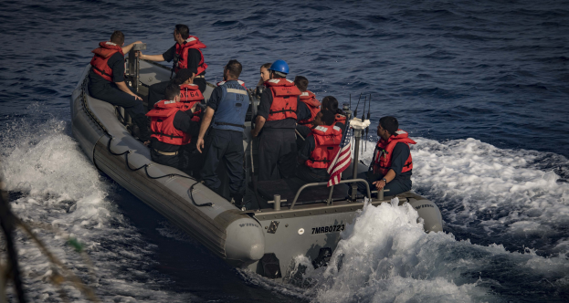 Menschen in Schwimmwesten und Helmen auf einem Boot im Wasser mit einem Seil auf der linken Seite.