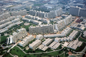 Luftaufnahme einer Stadt mit Gebäuden, Bäumen, Gras, Straßen, Fahrzeugen und einem hellblauen Swimmingpool, mit Condominiums in verschiedenen Formen und Größen.