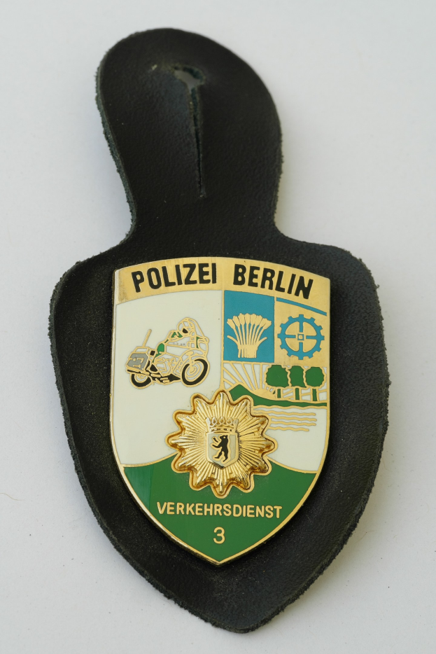 Ein schildförmiges Polizeisiegel mit der Aufschrift "Polizei Berlin" auf einem blauen Hintergrund, einem weißen Stern und einem weißen Rand, das auf einer Oberfläche liegt.