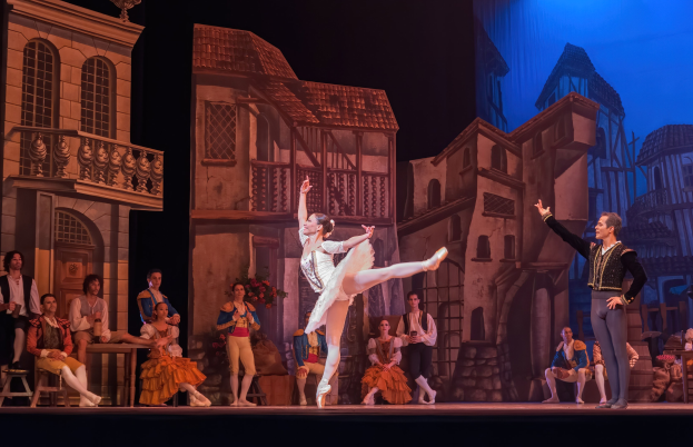 Zwei Tänzer performen auf der Bühne der Royal Opera House in London, mit einem Publikum im Hintergrund, das sitzt und steht.