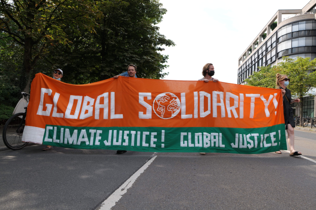 Gruppe von Menschen, die eine Straße mit einem "Globale Solidarität: Klimagerechtigkeit"-Schild entlanggehen, mit parkenden Fahrrädern und Gebäuden im Hintergrund.