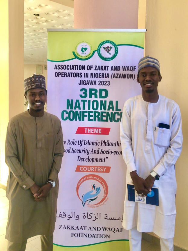 Zwei Männer stehen nebeneinander vor einem Banner "3. Nationaler Kongress" mit einer Säule und Deckenleuchten im Hintergrund.