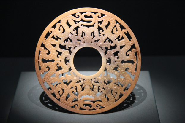 Ein chinesischer geschnitzter Jade-Teller in einem Museum ausgestellt, mit detaillierten Oberflächen-Schnitzereien und einem dunklen Hintergrund.