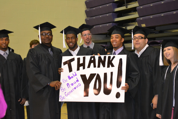 Eine Gruppe von Menschen steht in einer Reihe in der Mitte des Bildes, jeder hält ein Plakat mit den Worten "Danke" darauf.
