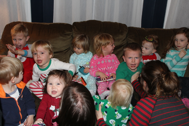 Eine Gruppe von Kindern sitzt auf einem Sofa in einem Raum, jeder hält ein Handy, mit einer Frau rechts daneben und einem Vorhang oben im Bild.