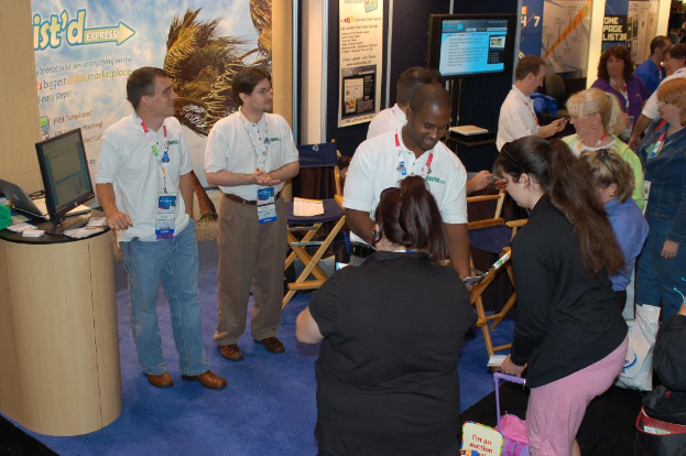 Eine Gruppe von Menschen, die in einem Raum mit einem Podium auf der linken Seite stehen, das ein Display an der Oberseite und Stühle auf dem Boden hat.