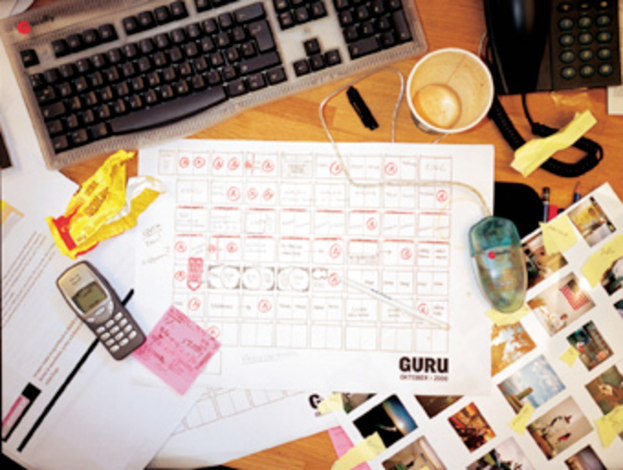 Ein chaotischer Schreibtisch mit Papieren, einem Computer, einem Telefon, Tassen und einem Mobiltelefon.