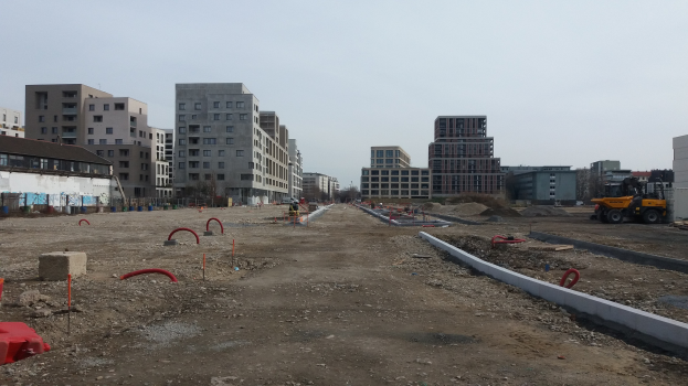 Baustelle mit schwerer Machinery, Gebäuden, Bäumen und einem klaren Himmel im Hintergrund.