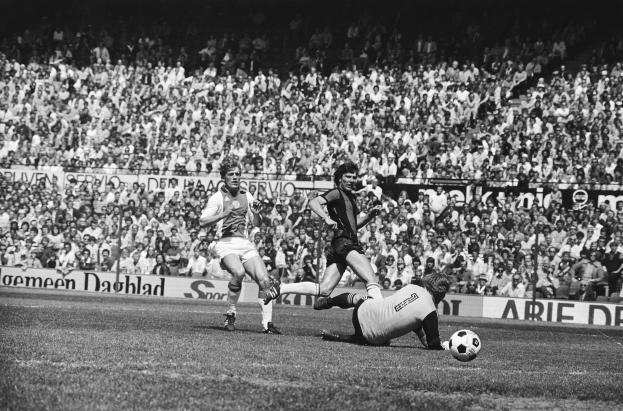 Schwarzes Foto von Füßtballspielern im Einsatz auf einem Feld mit Zuschauern im Hintergrund und einer Bundesliga 1978-79 Ajax 1-1 Hannover 96 Flagge.