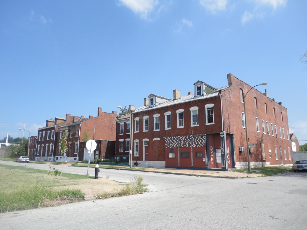 Ein Geb√§ude mit Masten und Stra√üenlaternen, umgeben von B√§umen und Fahrzeugen auf beiden Seiten, mit einem Weg, Gras und einem Feuerl√∂scher unten und dem Himmel oben.