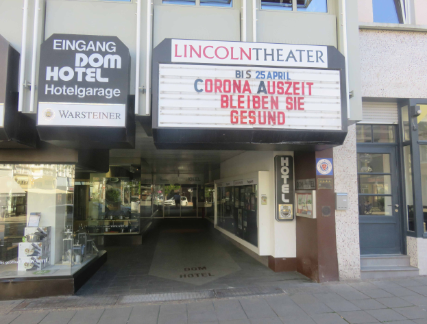 Das Lincoln Theater in Berlin, Deutschland, ein Gebäude mit Glasfenstern und -türen und einer Tafel mit Text darauf, zeigt verschiedene Gegenstände im Inneren und vermittelt den Eindruck einer pulsierenden Stadtlandschaft.