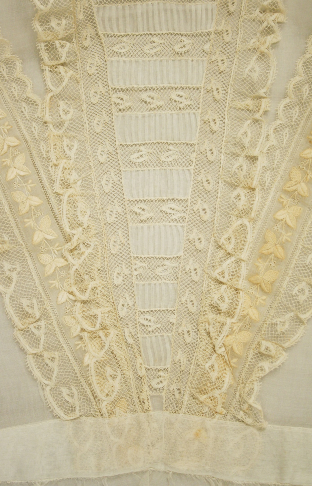 Nahaufnahme eines weißen Kleides mit detaillierter Spitzenverzierung, das feine Muster und einen leichten, luftigen Stoff für den Sommer bietet.