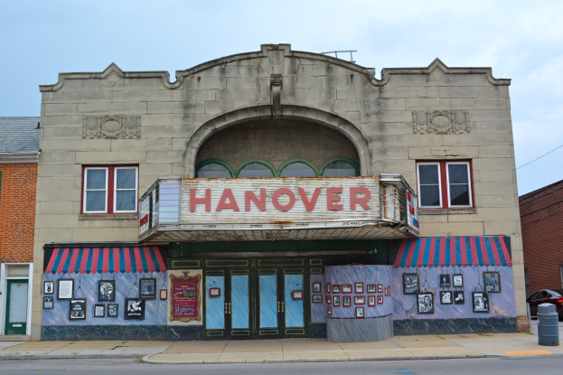 Außenansicht des Hanover Theatre in St. Louis, Missouri, mit Glasfenstern und -türen, einem Namensschild, Fotorahmen an der Wand, einem Mülleimer, einem Auto auf der Straße und einem bewölkten Himmel.