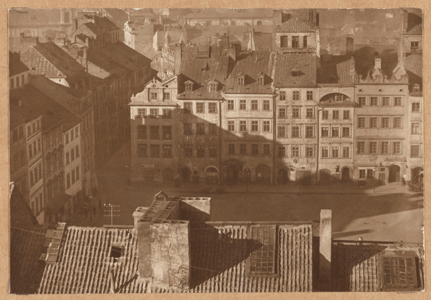 Ein altes Schwarz-Weiß-Foto einer Stadtlandschaft mit zahlreichen Gebäuden im Vordergrund und einer Straße in der Mitte, jedes Gebäude mit Fenstern.