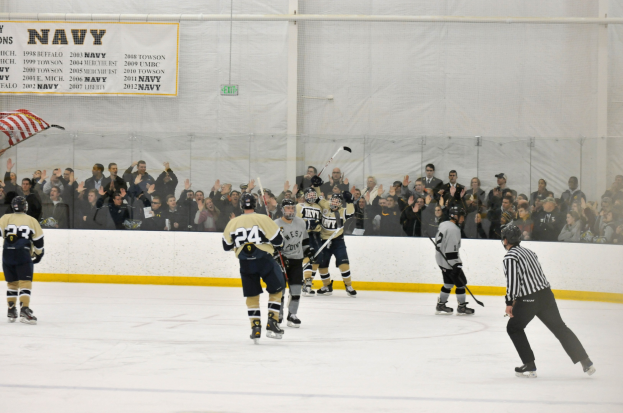 Eishockey-Spieler in Helmen und Uniformen konkurrieren auf einem Eisstadion mit Zuschauern in den Rängen und einer Bannerwand im Hintergrund.