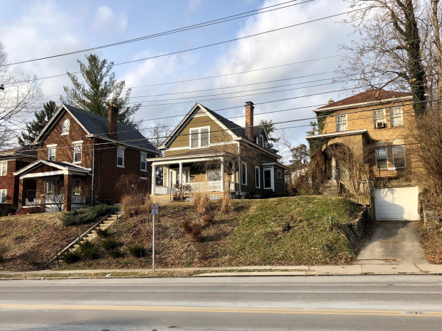 Reihe von Häusern entlang einer Straße mit Fenstern, Türen, Säulen, Geländern, Stufen, Pflanzen, Gras, Bäumen und einem Pfahl mit einer Tafel unter einem bewölkten Himmel, die eines der teuersten Häuser zum Verkauf in Detroit darstellt.