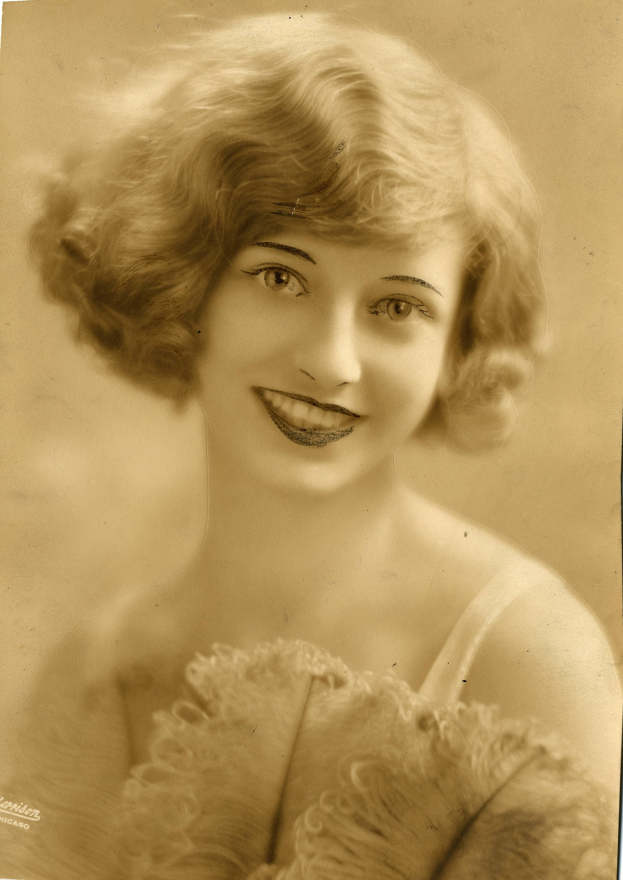 Ein Schwarz-Weiß-Foto einer Frau in einem Kleid im Stil der 1920er Jahre mit einem klassischen Bob-Haarschnitt, die warm lächelt.