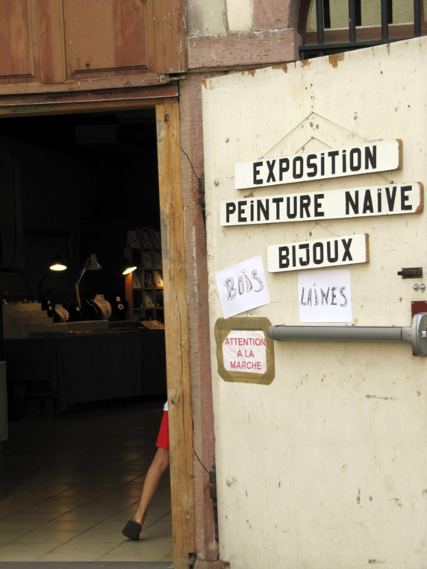 Ein Innenblick in einen Unterschlupf mit einer Person im Hintergrund neben Treppe und Lampen und einer Tür auf der rechten Seite mit Brettern und Text.