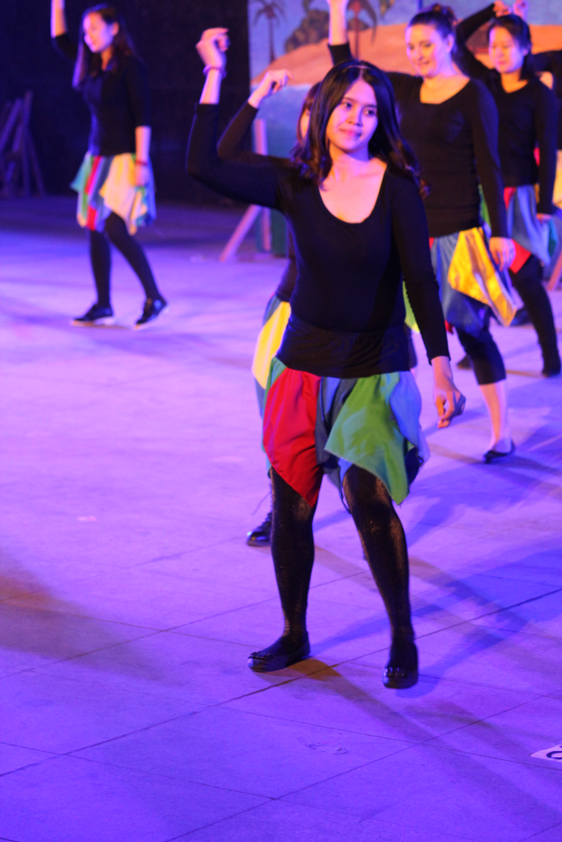 Eine Gruppe junger Frauen, die auf einer Bühne tanzen, mit einem Gemälde im Hintergrund, alle tragen Schuhe.