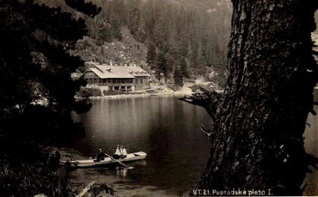 Ein Schwarz-Weiß-Foto von zwei Menschen in einem Kanu auf einem See, Paddel in der Hand, mit Bäumen und einem Haus im Hintergrund, aufgenommen in Popradskie, Polen, in den 1920er Jahren.