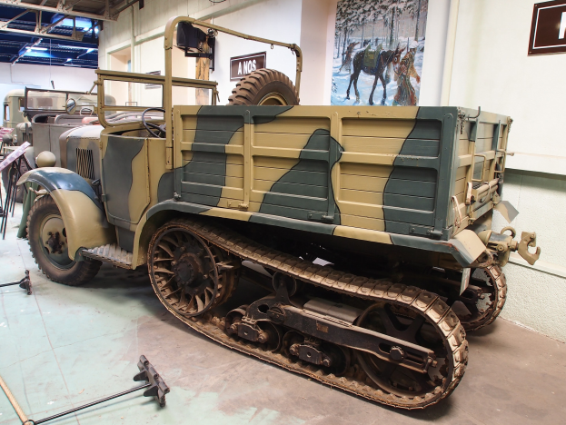 Alter militärischer M3A1-Spähwagen im Museum ausgestellt zwischen anderen Fahrzeugen, mit informativen Schildern und Deckenbeleuchtung.