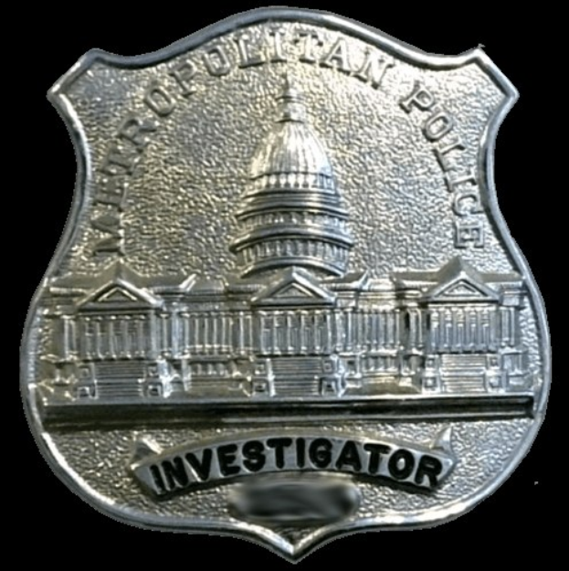 Ein silbernes Polizeiabzeichen mit der Aufschrift "Ermittler" auf einem weißen Hintergrund.