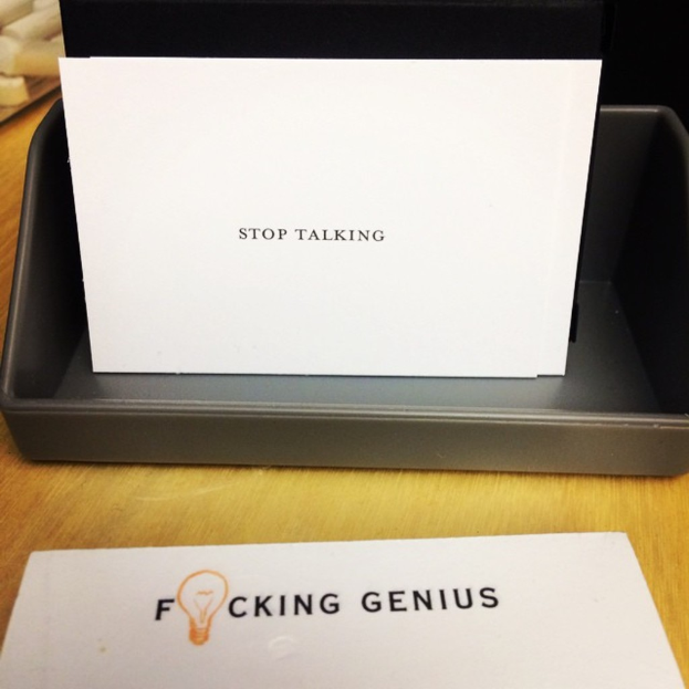 Ein Druckerbox mit einem Blatt Papier darauf, auf dem steht: "Hör auf zu reden" und ein weiteres Blatt auf dem Tisch, auf dem steht: "Verdammte Genies."