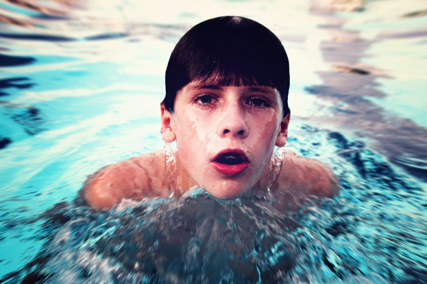 Ein Junge, der in der Mitte eines Gewässers schwimmt.